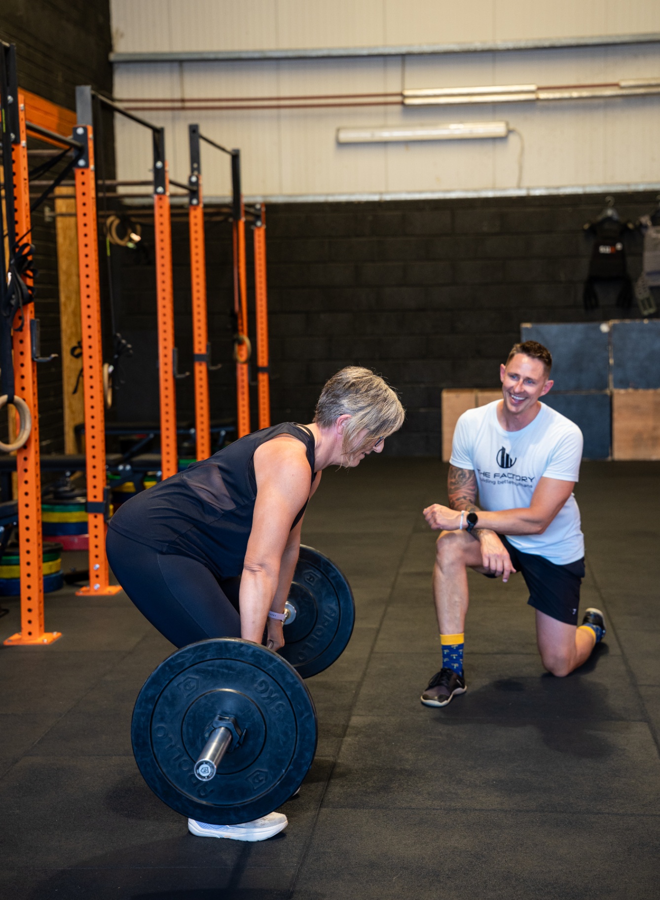 Coach smiling while client deadlifts a barbell