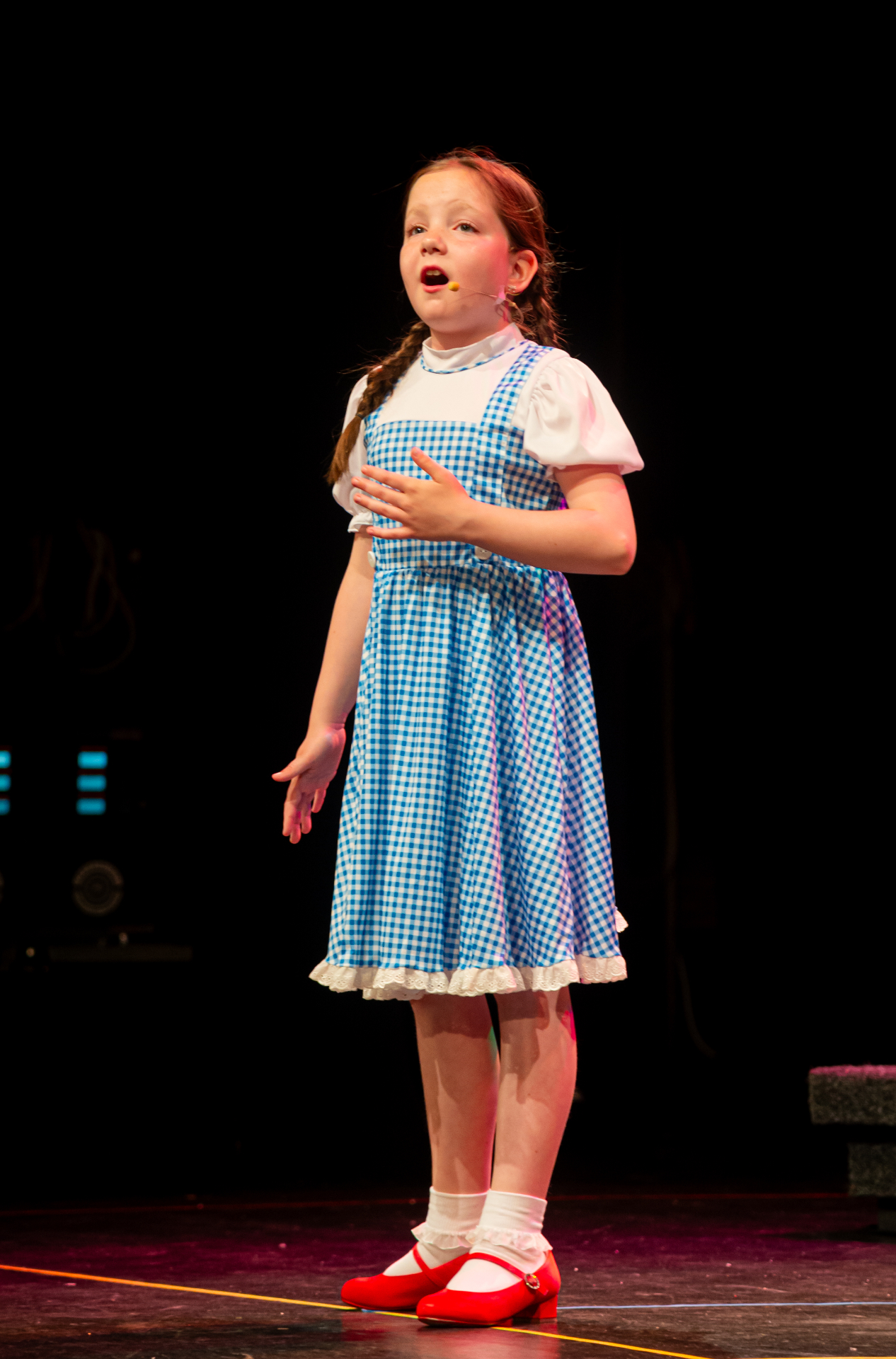 Young performer in gingham dress singing on stage