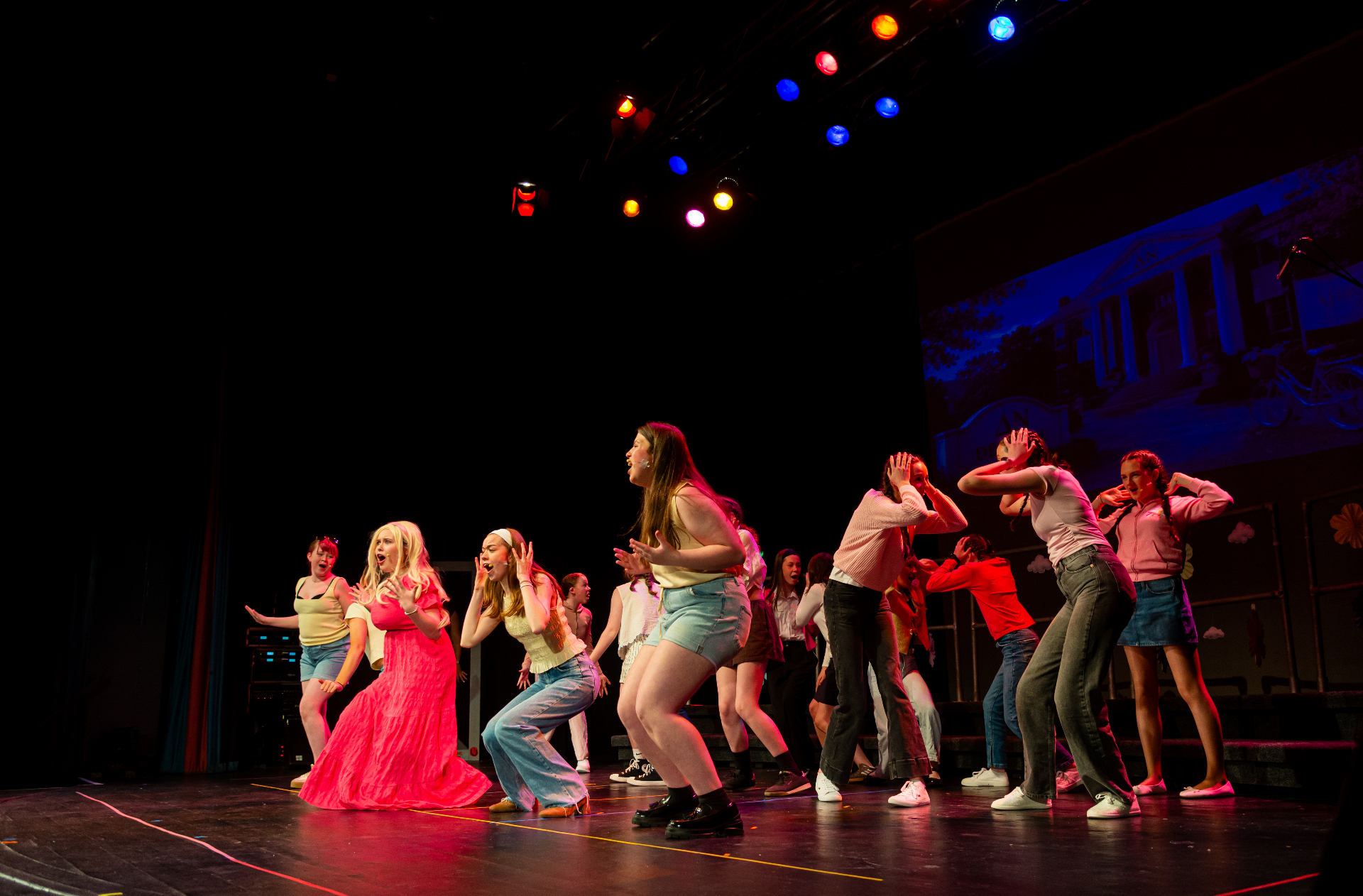 Ensemble cast dancing on stage under colorful lights