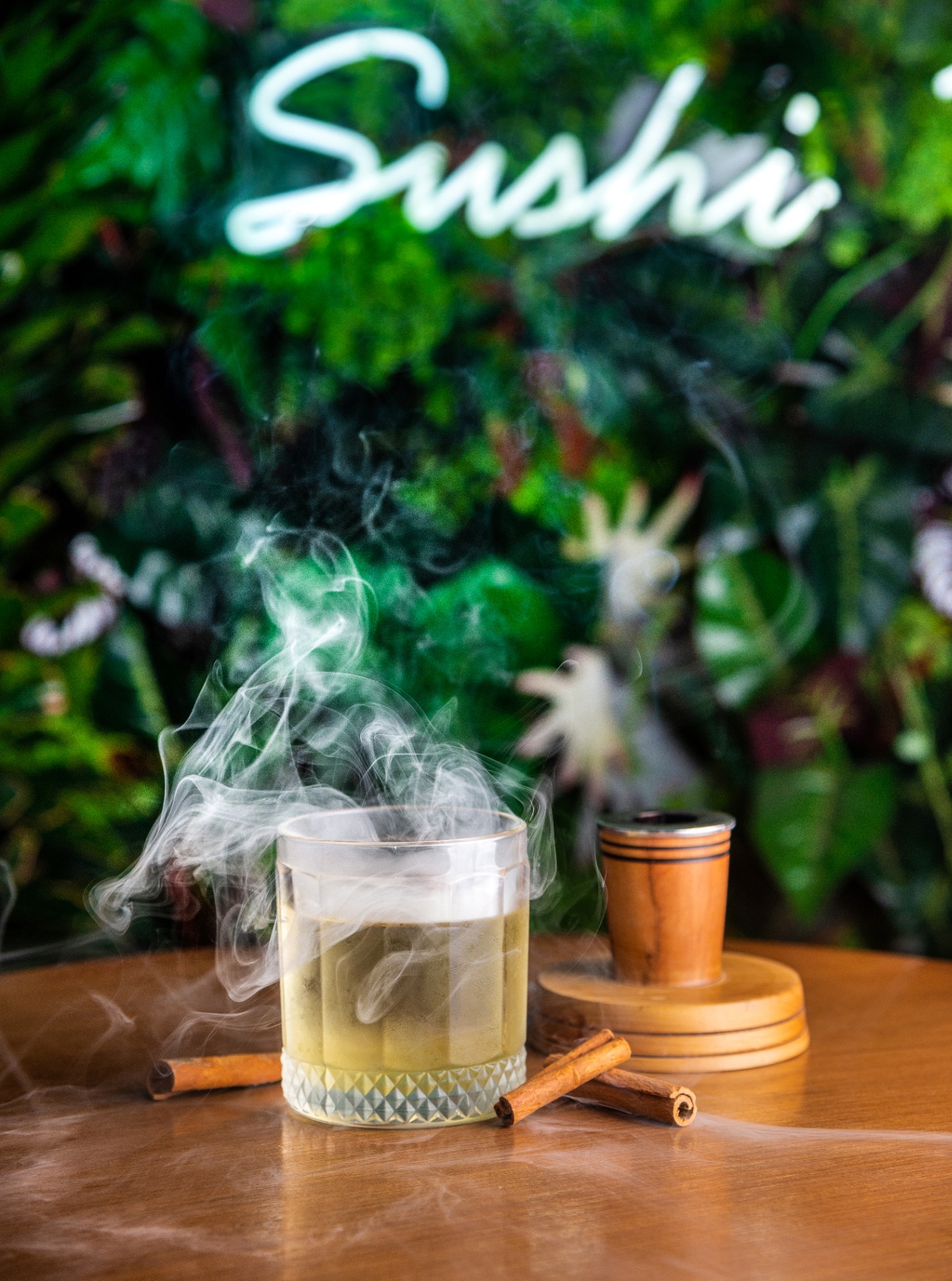 Steaming cocktail on a wooden table with cinnamon and soft greenery in the background