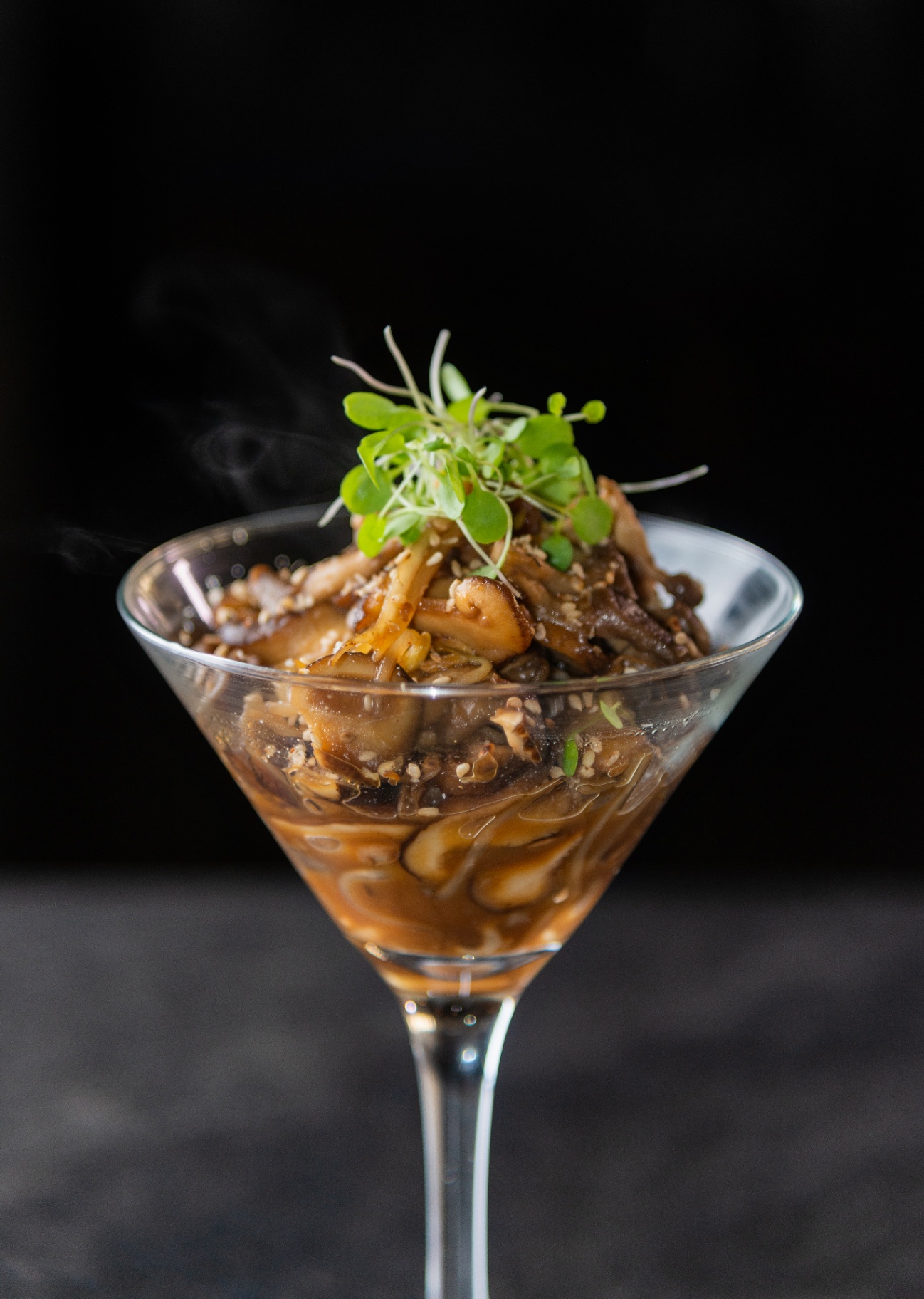 Savory mushroom dish served in a martini glass with microgreens against a dark background
