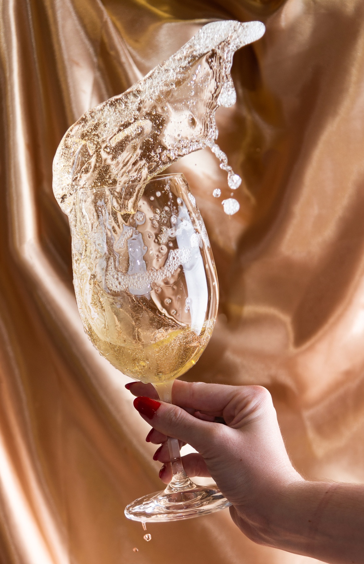 Sparkling wine splash frozen above a glass held by hand against a satin backdrop