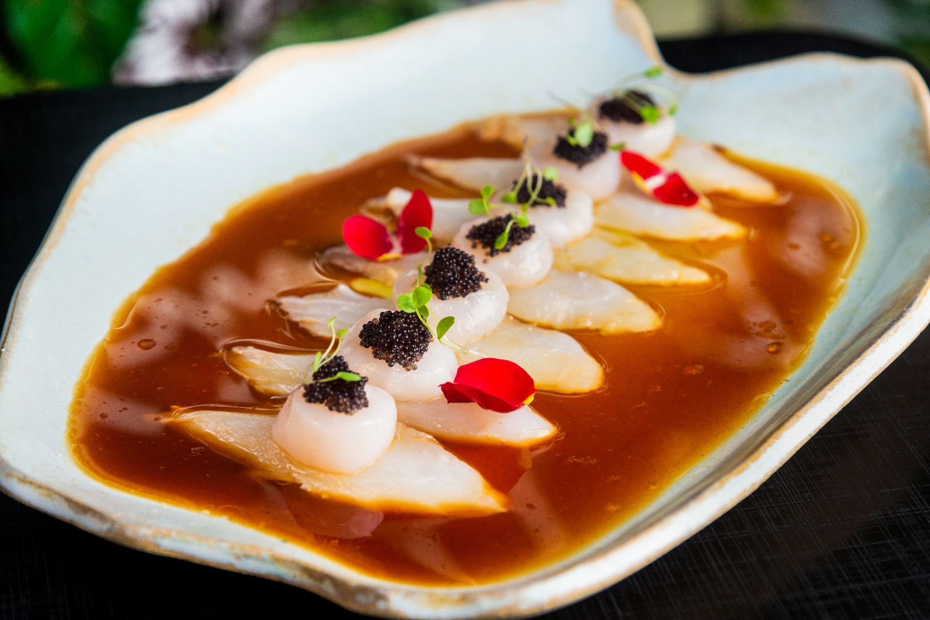 Refined plated seafood dish with dark caviar and flower petals in warm sauce