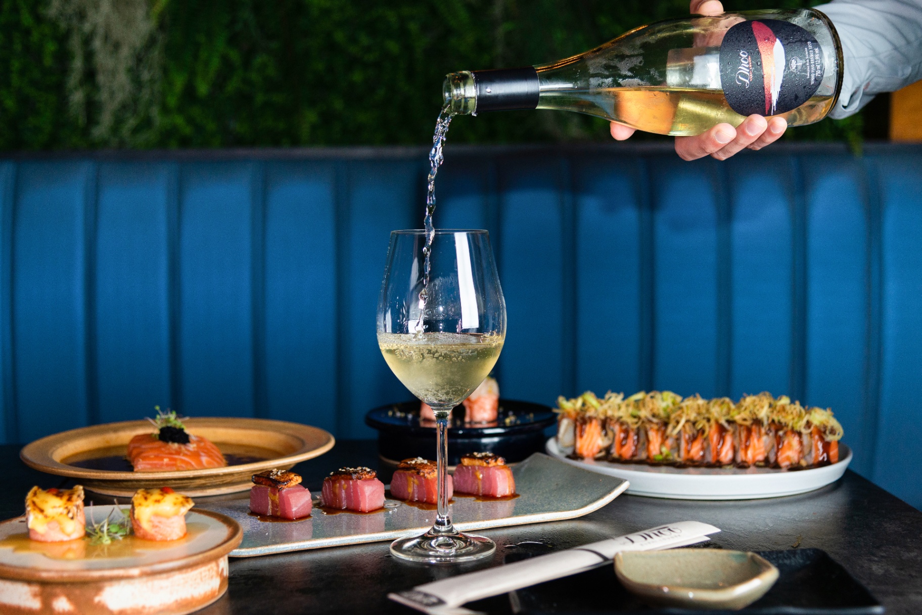 White wine being poured into a glass alongside plated sushi dishes