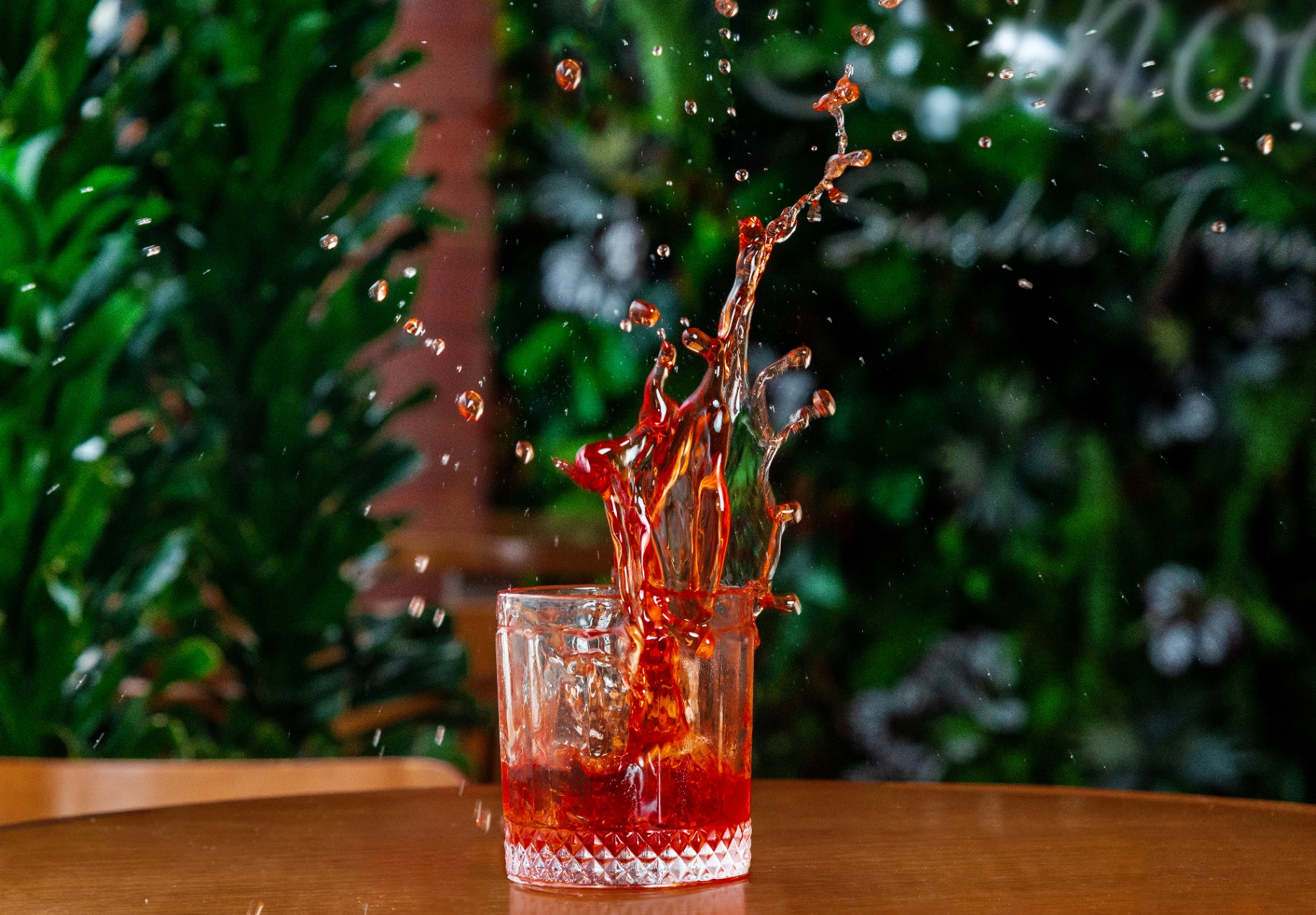 Red cocktail splash captured midair in a crystal glass with leafy backdrop