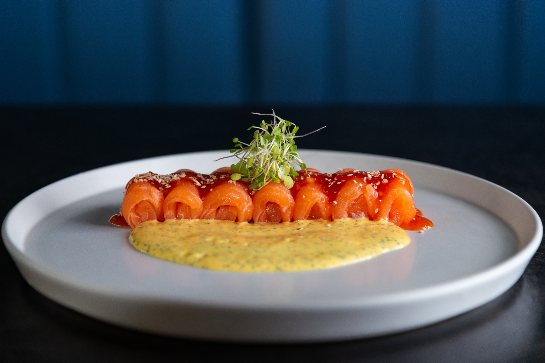 Salmon rolls topped with sesame and red sauce, served with mustard cream on a white plate