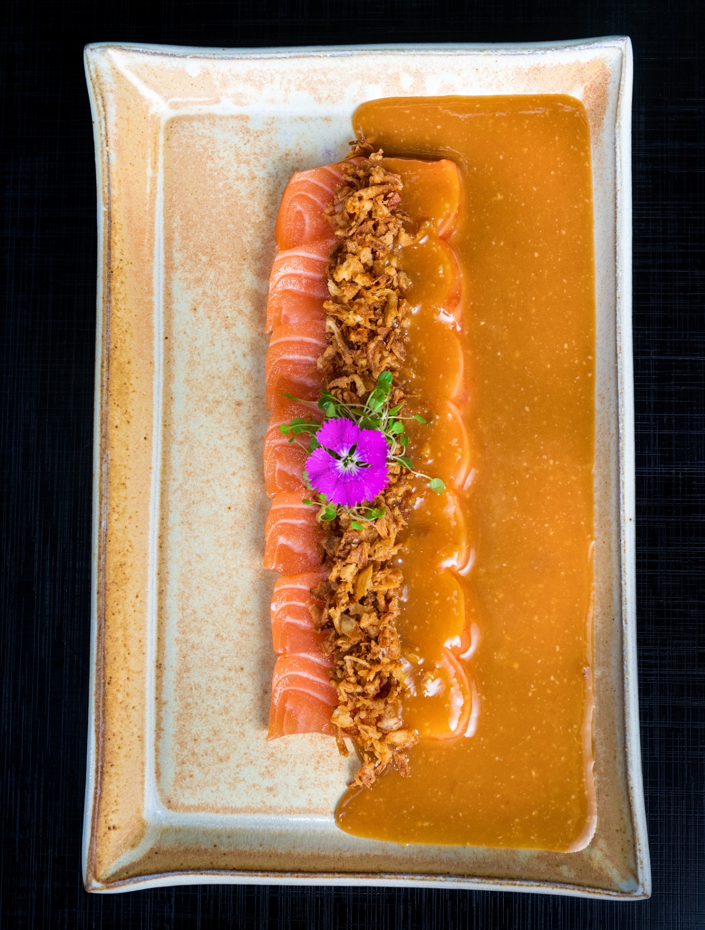 Sashimi salmon with crispy onions and orange sauce on a rustic rectangular plate
