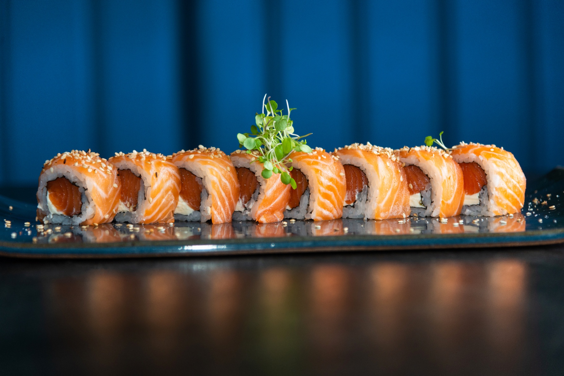 Sushi rolls with salmon and sesame arranged in a line on a blue plate