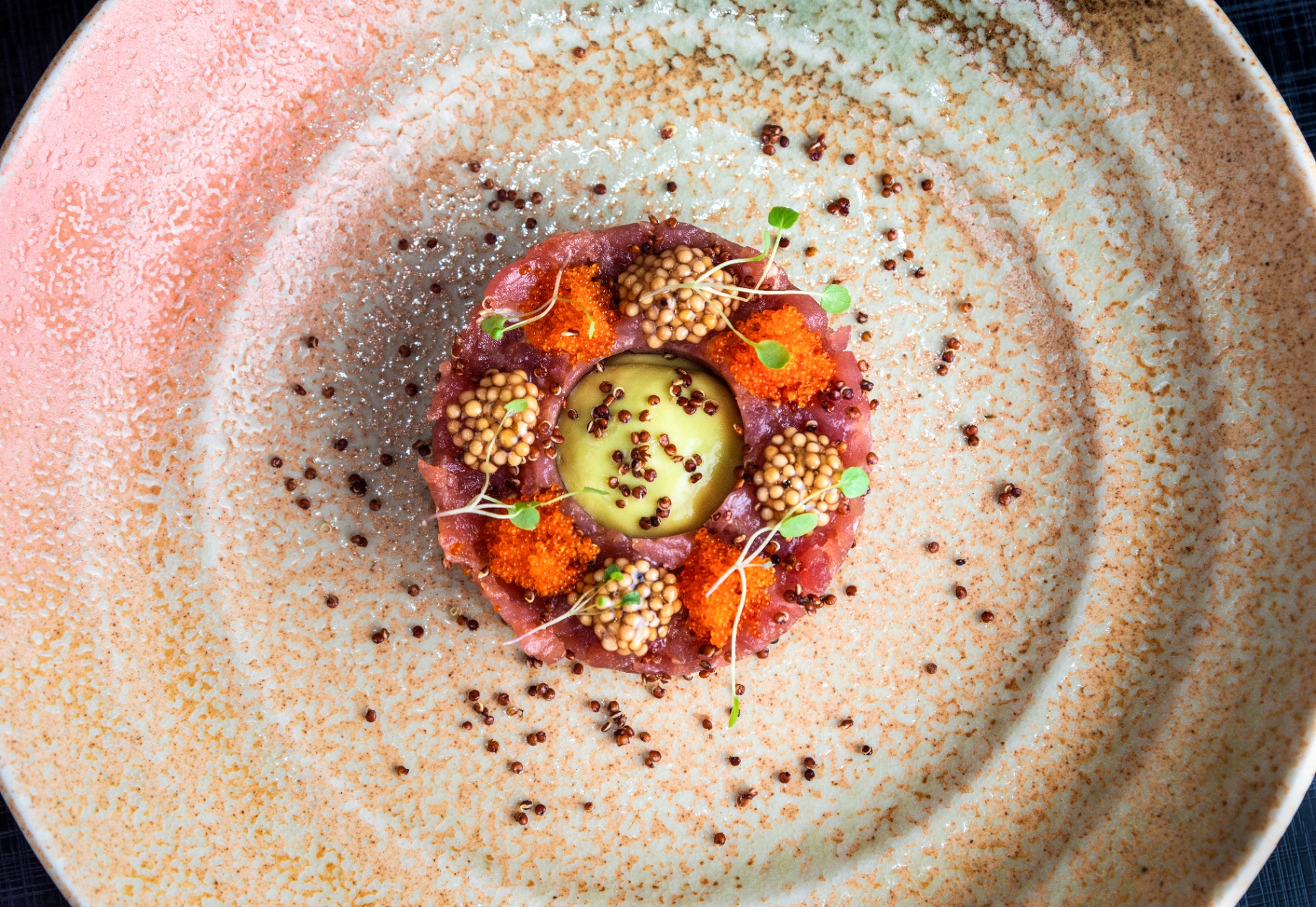 Tuna tartare ring with tobiko and mustard pearls on a speckled ceramic plate