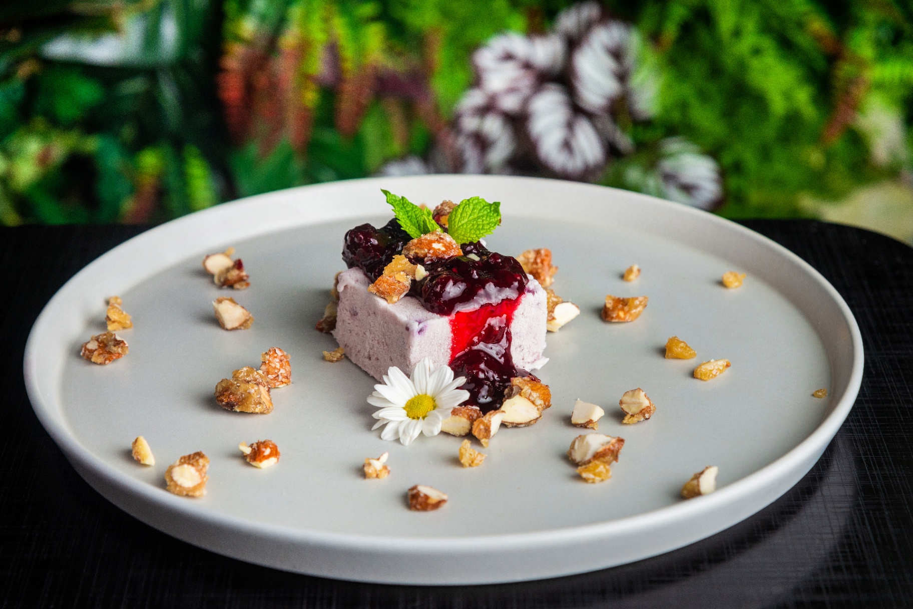 Berry parfait dessert with jam, mint, and caramelized nuts on a grey plate
