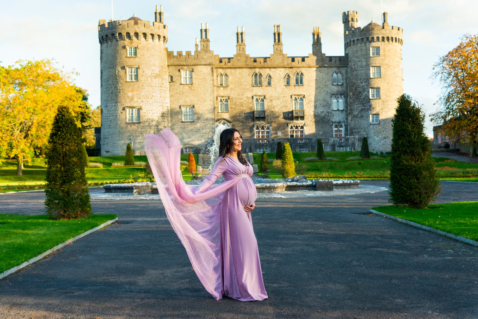 Pregnant woman in a flowing lilac gown in front of a castle
