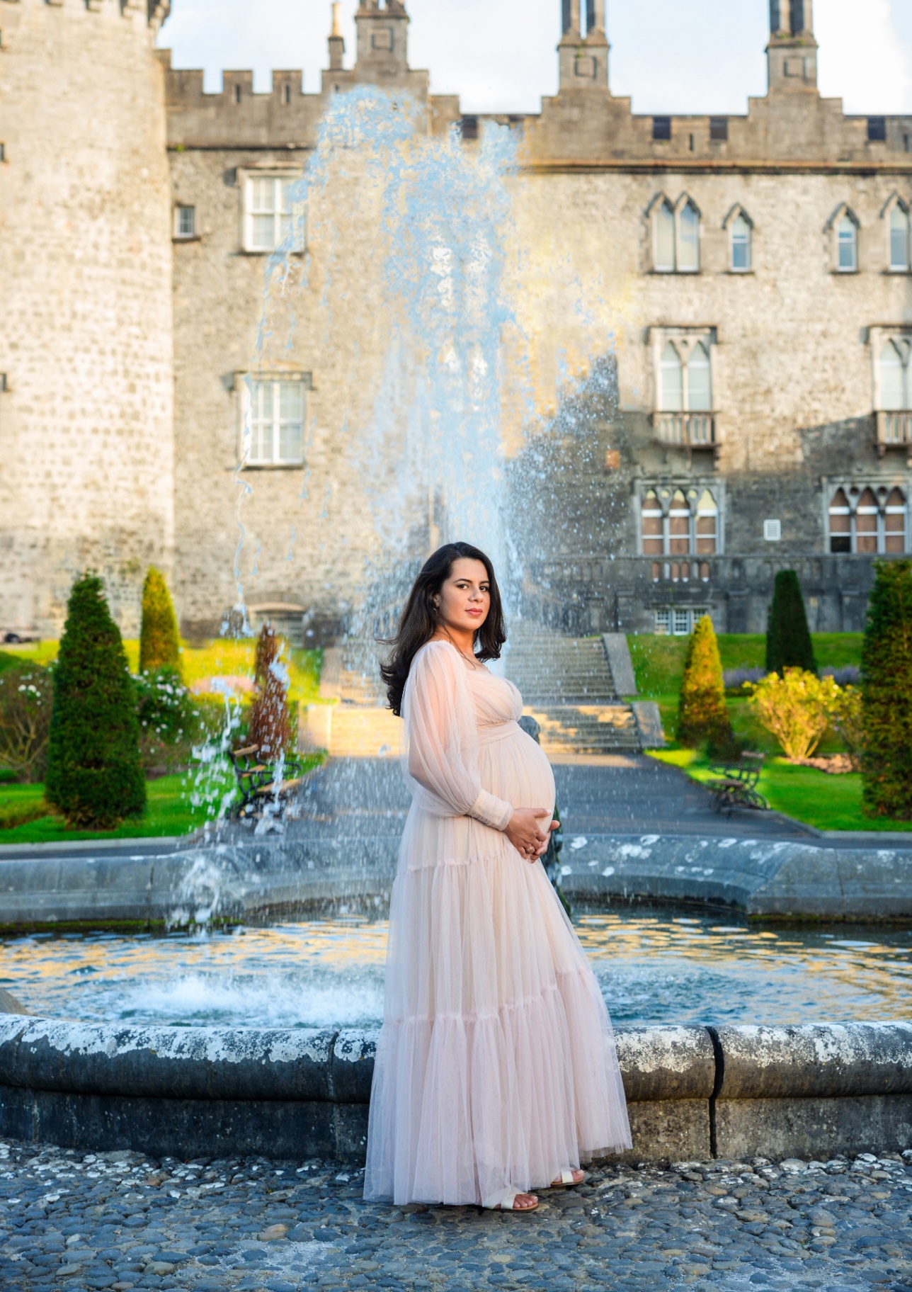 Pregnant woman posing by a fountain with a castle backdrop