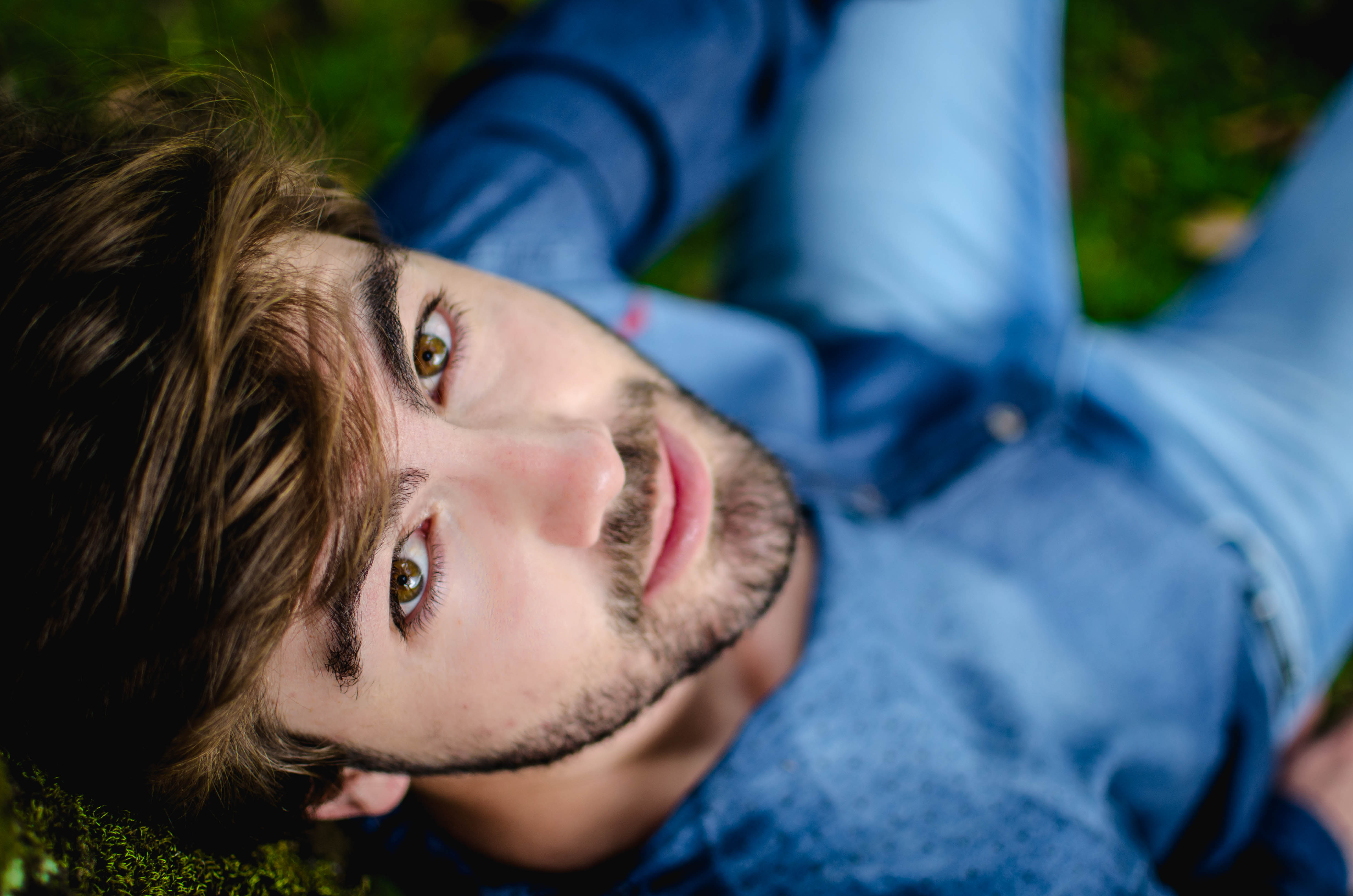 Man with brown hair and beard lying in the grass in a denim shirt