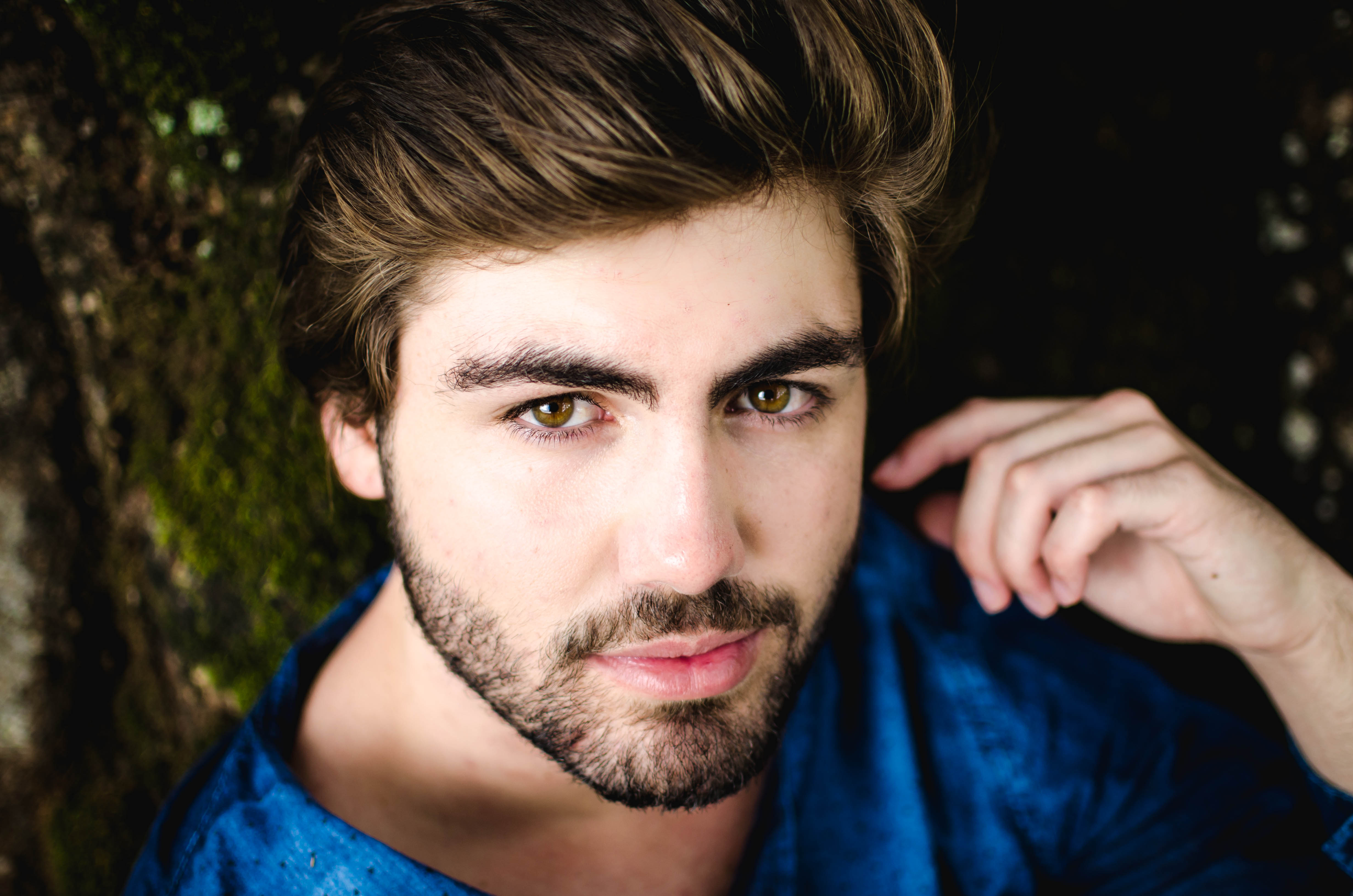 Portrait of a man in a blue shirt leaning against a mossy tree