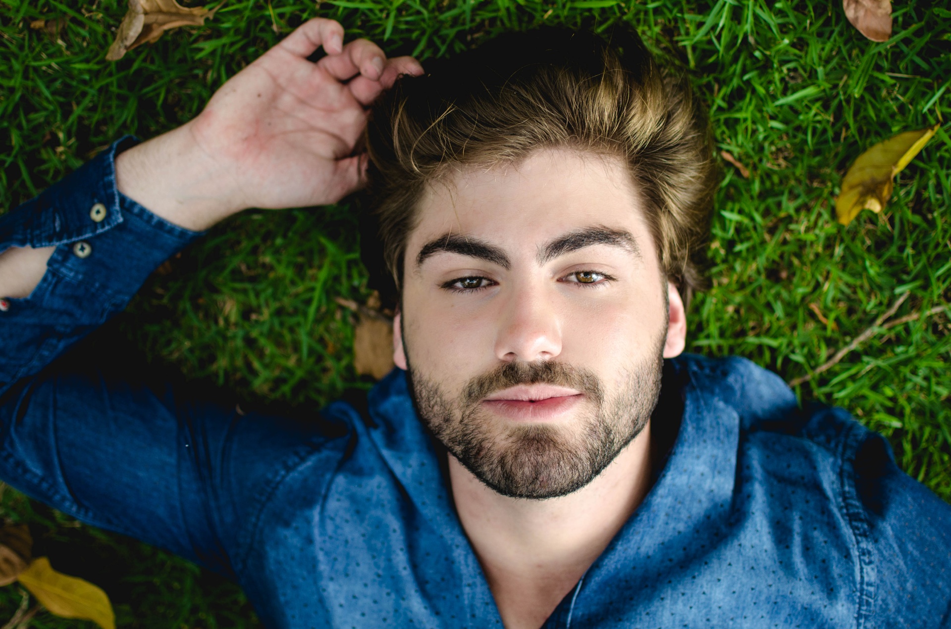 Man in a denim shirt lying on the grass with autumn leaves