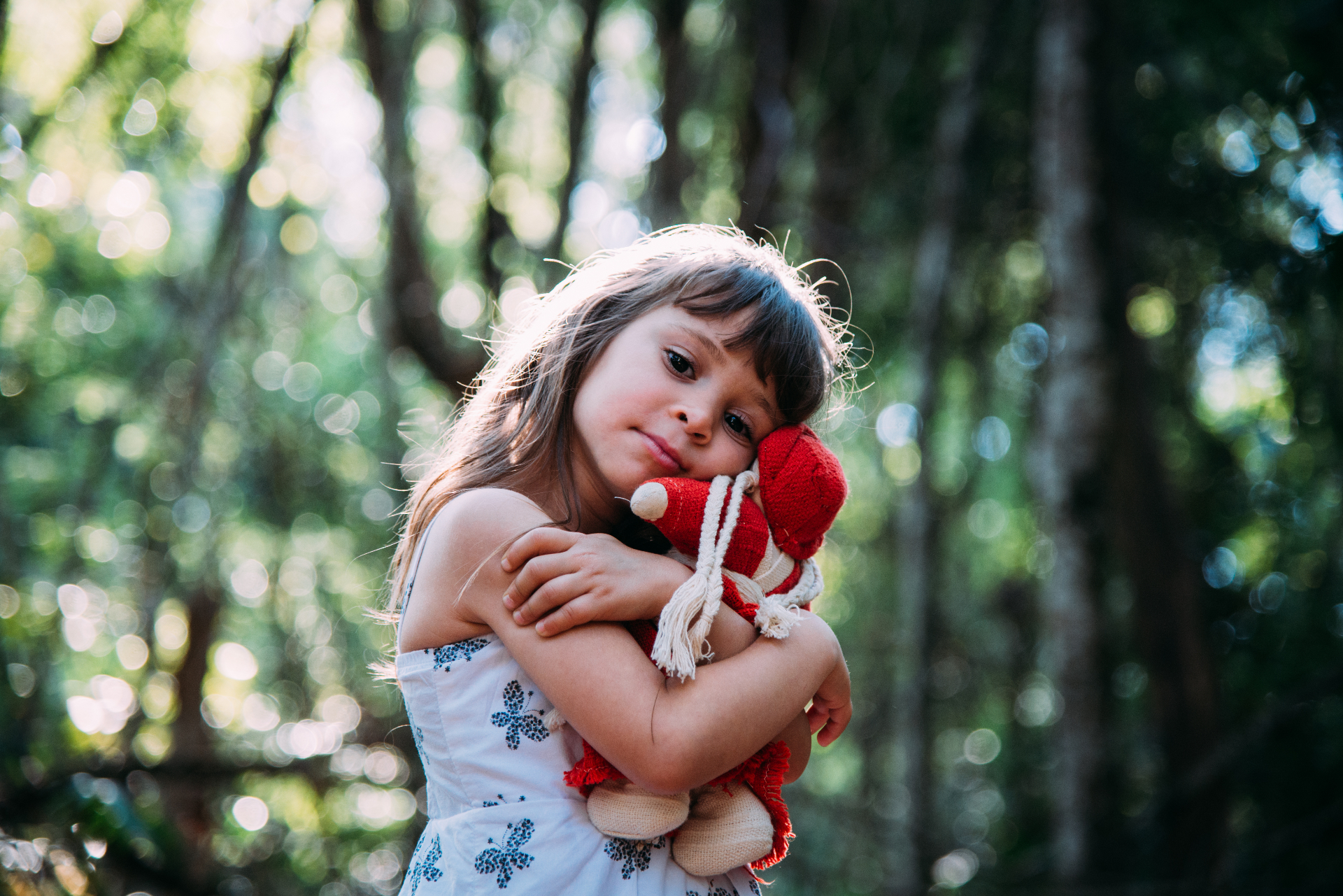 Child holding a red doll in a sunlit forest